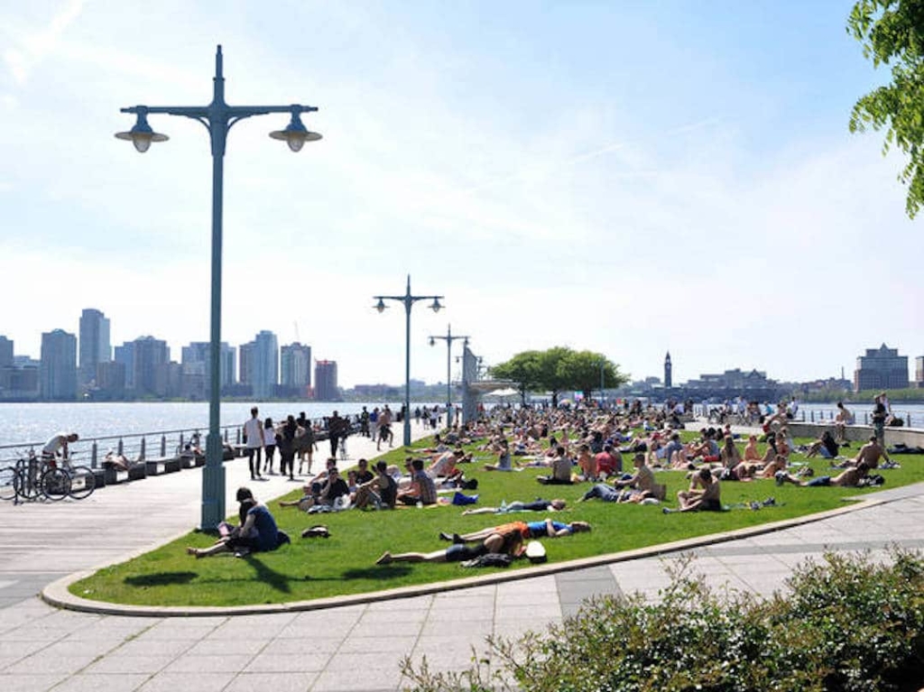 Vue sur le Hudson River Park, avec de nombreuses personnes assises sur l'herbe face à la rivière.