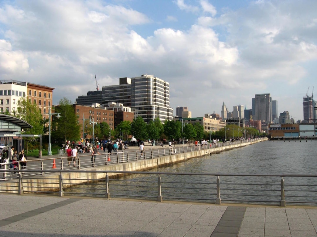 Vue sur le Hudson River Park. Il y a des personnes qui marchent le long de la rivière et des buildings à l'arrière plan.